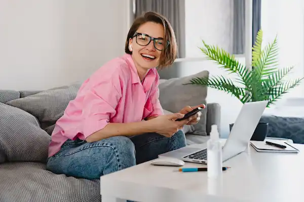 smiling woman pink shirt sitting relaxed sofa home table working online laptop from home 1 scaled min Recruitment & Selection Service